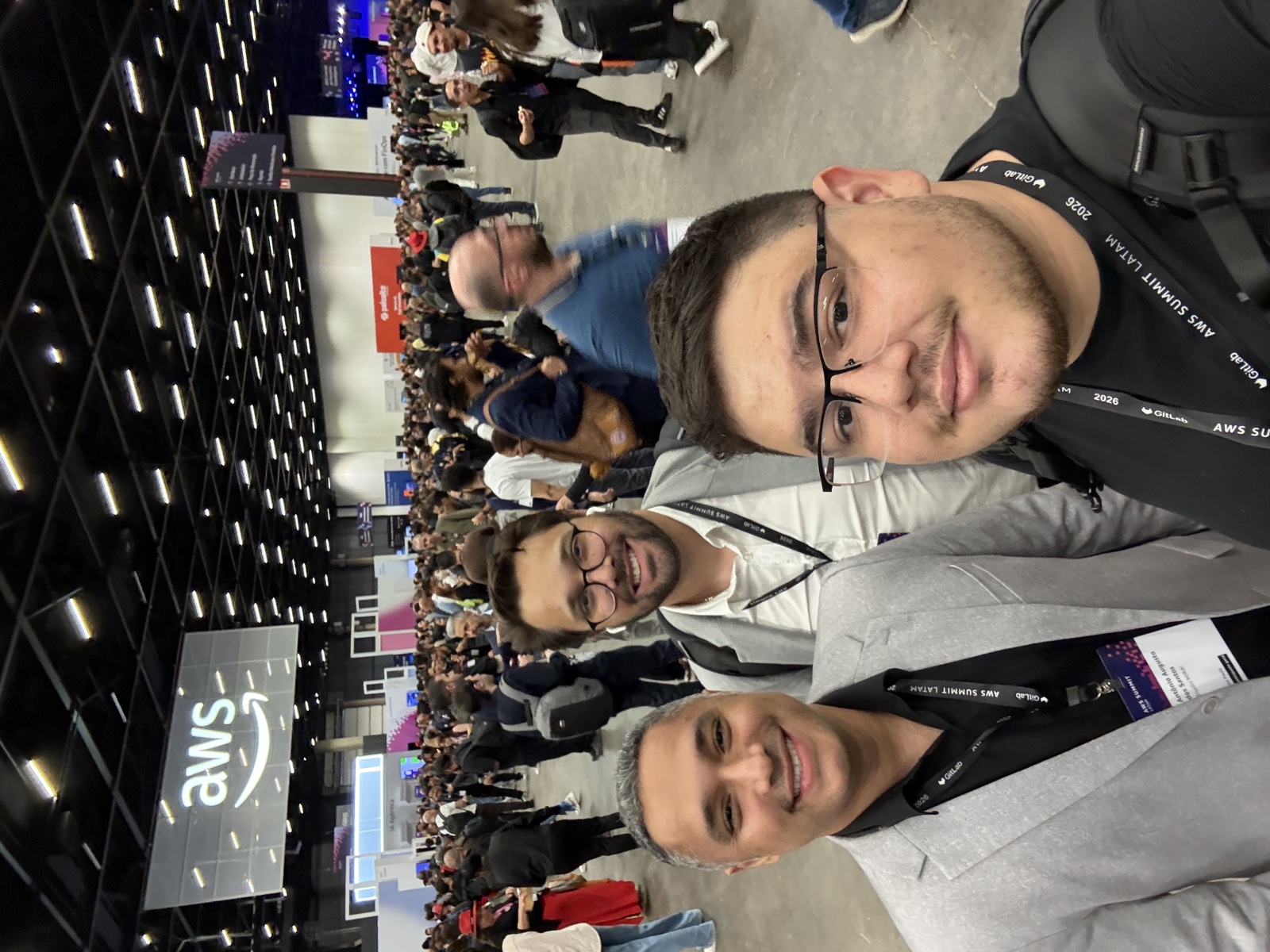 Registro da presença da Infinita no evento da AWS, com três participantes em primeiro plano e a marca AWS ao fundo.